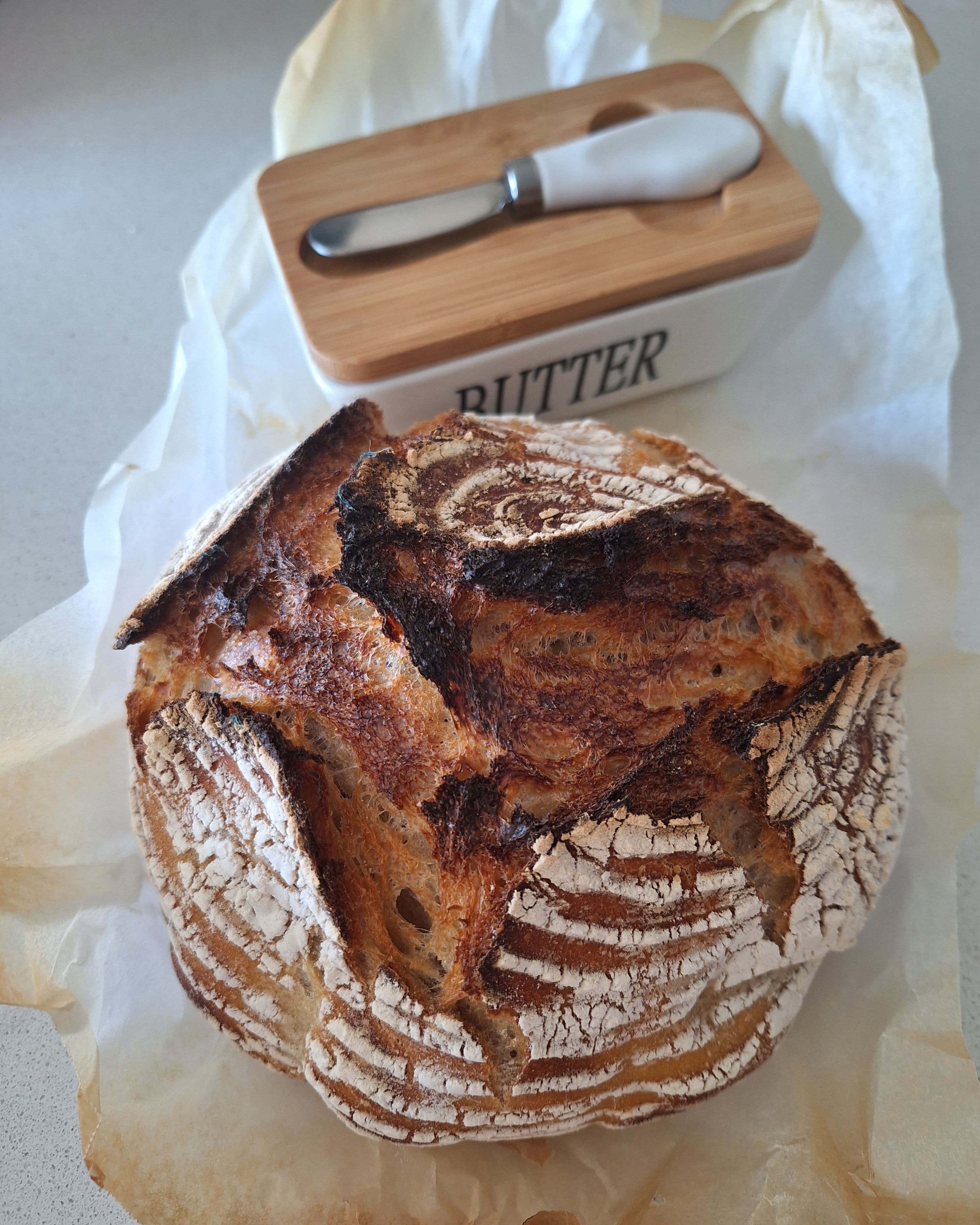 A homemade loaf on baking paper beside a butter dish